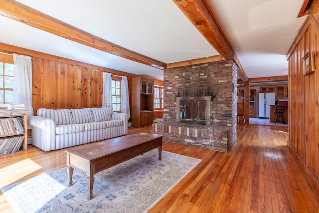 living room featuring wood walls, hardwood / wood-style floors, beamed ceiling, and a brick fireplace