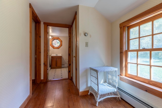 hall featuring hardwood / wood-style floors, baseboard heating, and lofted ceiling