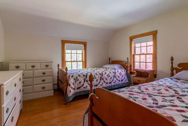 bedroom featuring light hardwood / wood-style floors, lofted ceiling, baseboard heating, and multiple windows