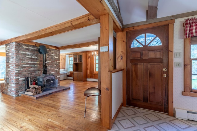 entrance foyer featuring beam ceiling, a wood stove, baseboard heating, and light hardwood / wood-style flooring