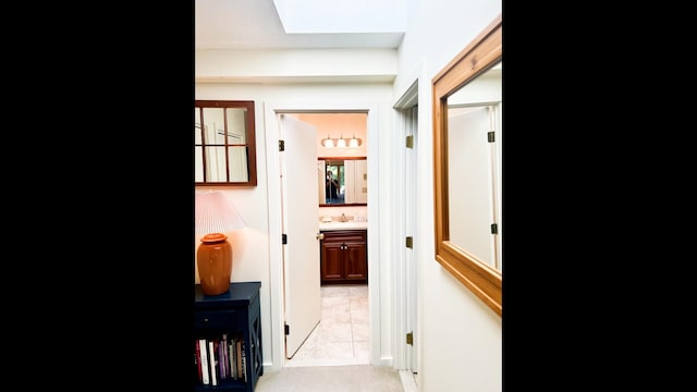 hallway with light colored carpet, a skylight, and sink