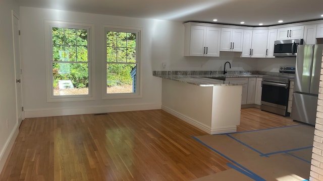 kitchen featuring white cabinets, appliances with stainless steel finishes, light stone counters, and hardwood / wood-style flooring