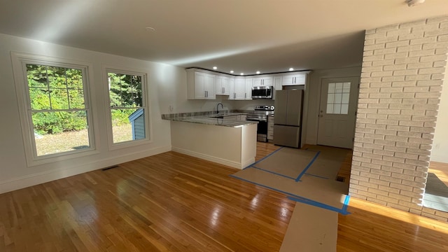 kitchen with appliances with stainless steel finishes, kitchen peninsula, white cabinetry, and light wood-type flooring