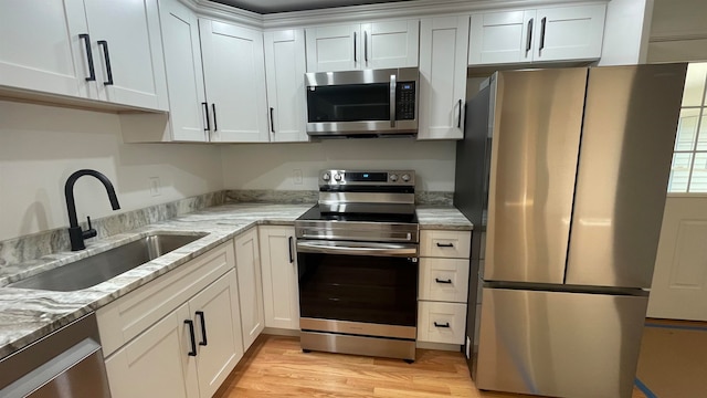 kitchen featuring light stone countertops, sink, light hardwood / wood-style floors, white cabinetry, and appliances with stainless steel finishes