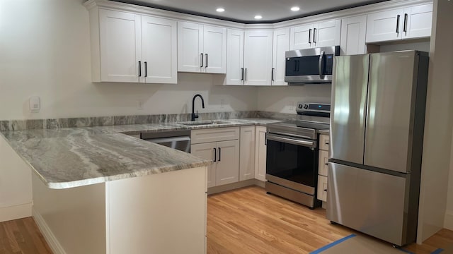 kitchen featuring white cabinets, sink, light hardwood / wood-style flooring, stainless steel appliances, and light stone countertops