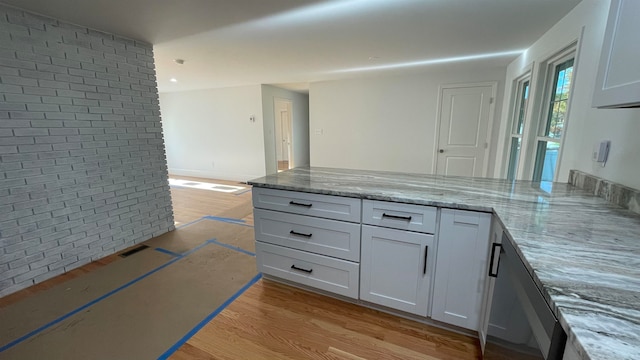 kitchen with light stone counters, brick wall, light hardwood / wood-style floors, and white cabinetry