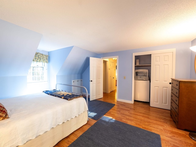 bedroom with vaulted ceiling, light hardwood / wood-style flooring, a textured ceiling, and washer / dryer