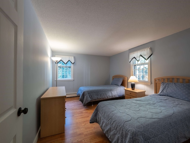 bedroom with a baseboard radiator, light wood-type flooring, and a textured ceiling