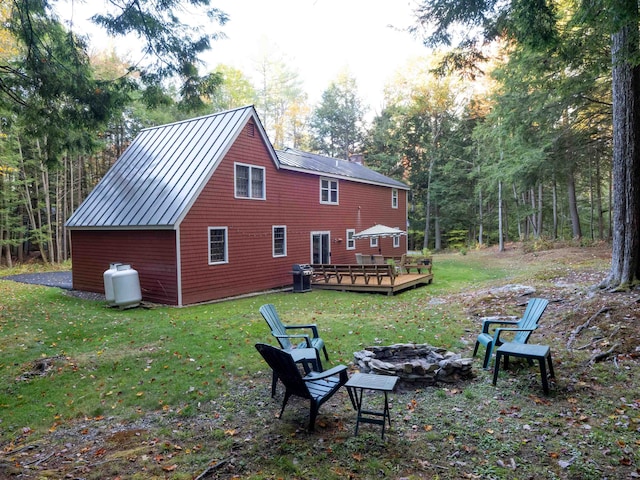 rear view of house with a wooden deck, a lawn, and an outdoor fire pit