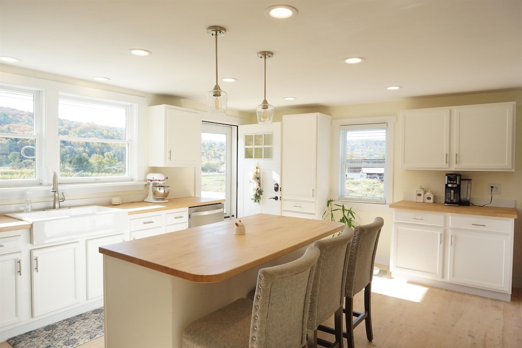 kitchen featuring white cabinets, a sink, a center island, butcher block counters, and decorative light fixtures