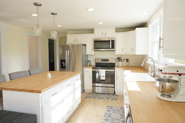 kitchen featuring butcher block countertops, sink, hanging light fixtures, stainless steel appliances, and white cabinets