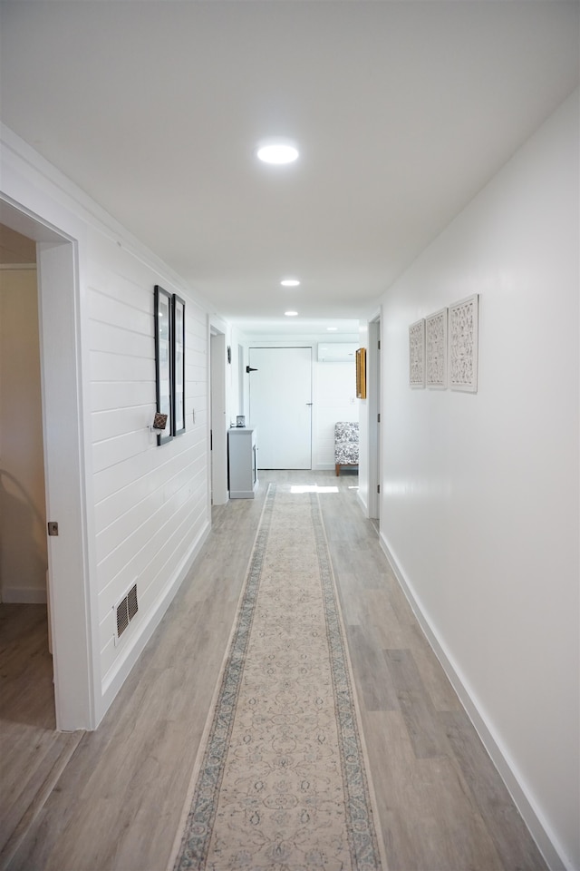 hall with light hardwood / wood-style floors and an AC wall unit