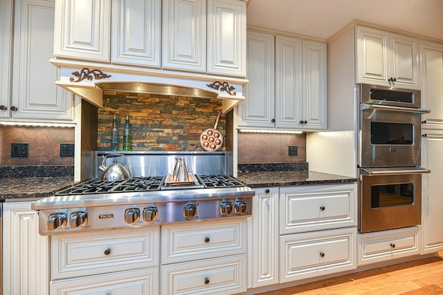 kitchen with tasteful backsplash, dark stone countertops, appliances with stainless steel finishes, and light wood-type flooring