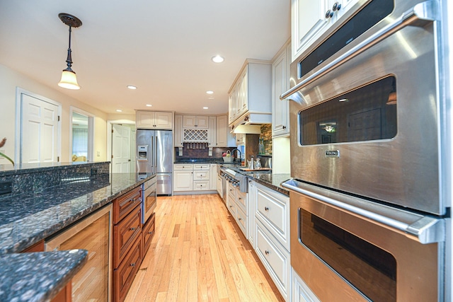 kitchen with stainless steel appliances, dark stone counters, pendant lighting, and light wood-type flooring