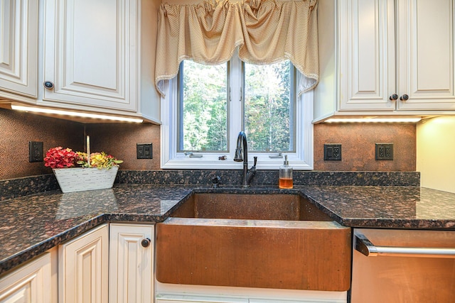 kitchen with dark stone counters, white cabinetry, stainless steel dishwasher, and sink