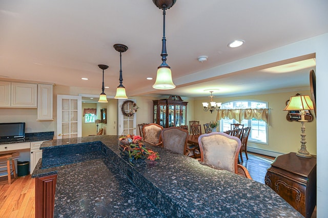 kitchen with light hardwood / wood-style floors, a notable chandelier, dark stone counters, a baseboard radiator, and decorative light fixtures