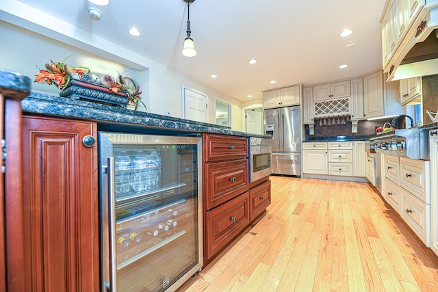 kitchen featuring wine cooler, hanging light fixtures, backsplash, appliances with stainless steel finishes, and light hardwood / wood-style floors