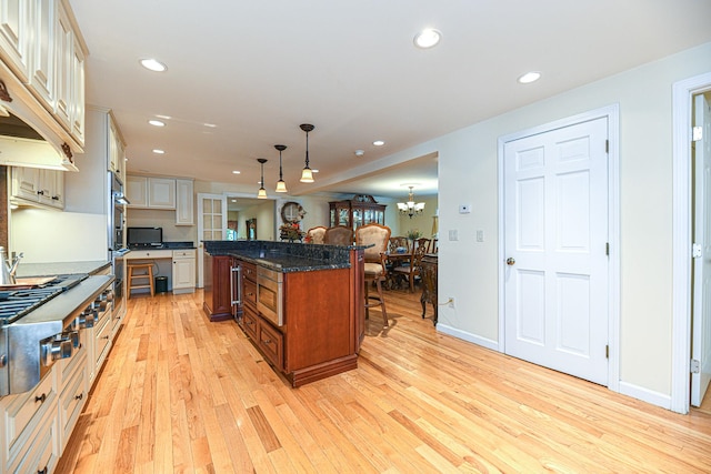 kitchen with a breakfast bar area, light hardwood / wood-style flooring, stainless steel appliances, hanging light fixtures, and a spacious island