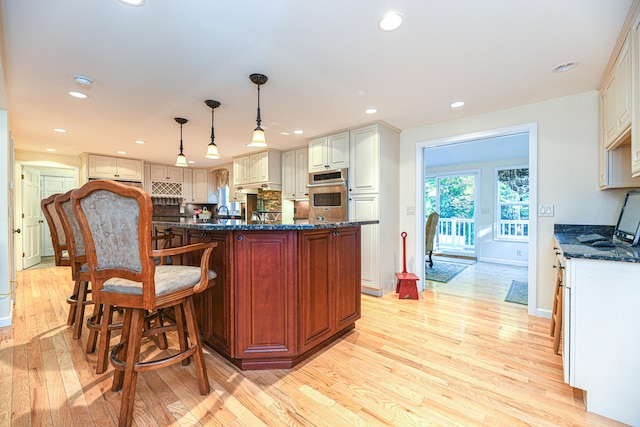 kitchen with pendant lighting, white cabinets, oven, and light wood-type flooring