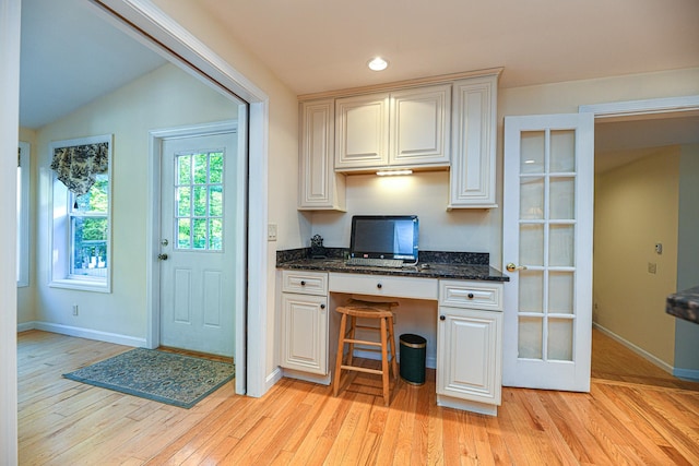 kitchen with light hardwood / wood-style flooring, dark stone countertops, vaulted ceiling, built in desk, and a kitchen bar