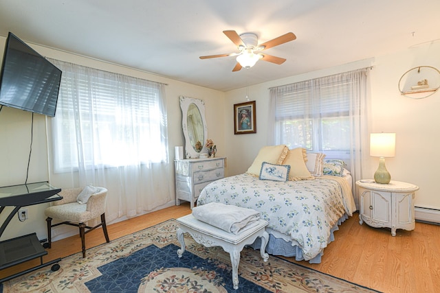 bedroom with ceiling fan, a baseboard heating unit, and light hardwood / wood-style floors