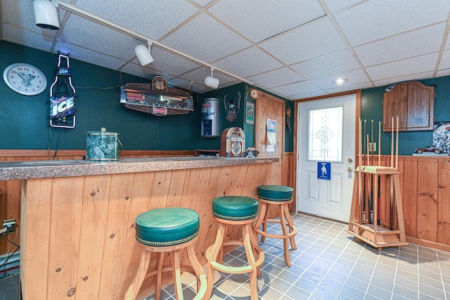 bar with a drop ceiling, wooden walls, and light tile patterned floors