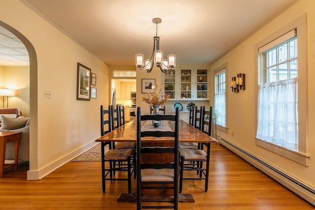 dining room featuring ornamental molding, light wood-type flooring, a notable chandelier, and a baseboard heating unit