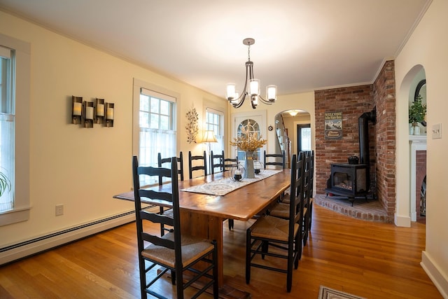 dining area featuring wood-type flooring, crown molding, an inviting chandelier, and a wood stove