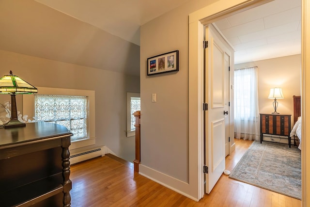 hallway with light hardwood / wood-style flooring, a baseboard heating unit, and a wealth of natural light