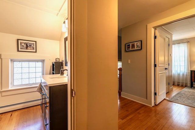 hall featuring a baseboard heating unit, hardwood / wood-style flooring, and sink