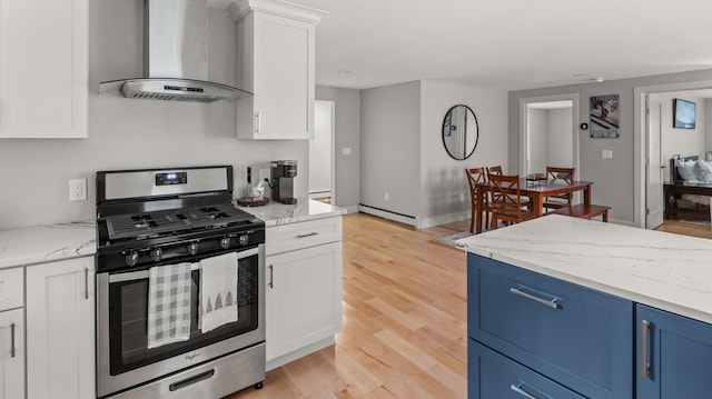 kitchen featuring wall chimney range hood, light wood-type flooring, blue cabinetry, stainless steel gas range, and a baseboard heating unit