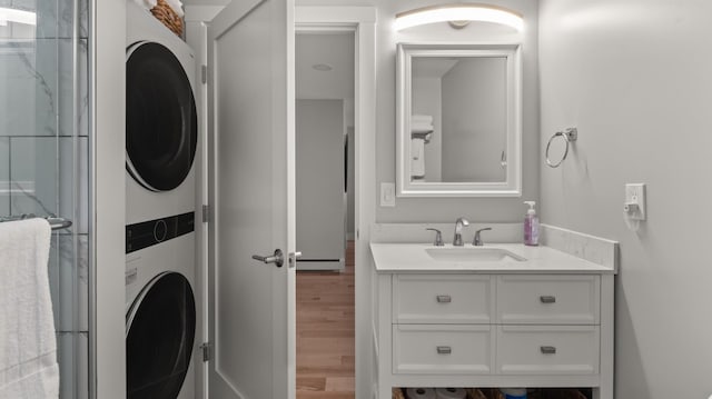 clothes washing area featuring hardwood / wood-style flooring, stacked washer / dryer, and sink