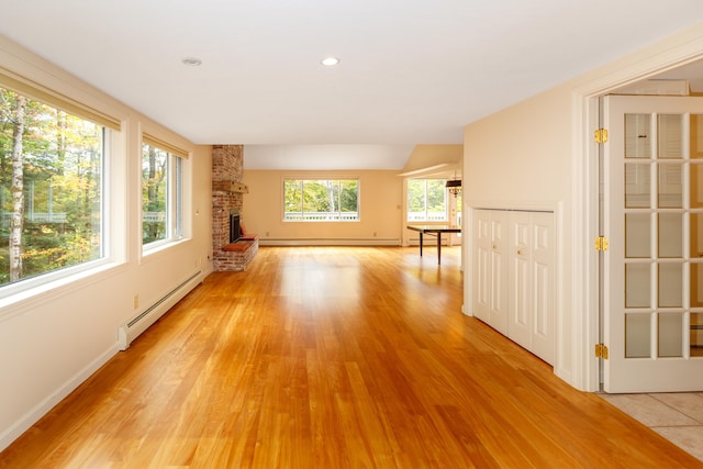 spare room with a fireplace, plenty of natural light, baseboard heating, and light wood-type flooring