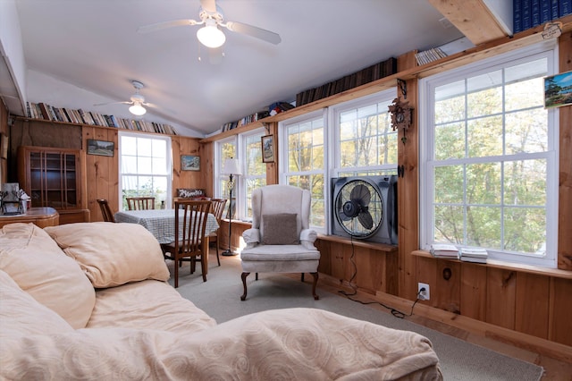 carpeted living room with ceiling fan, wooden walls, and vaulted ceiling