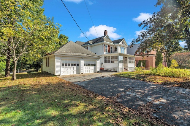 view of front facade featuring a garage, a front lawn, an outdoor structure, and a sunroom