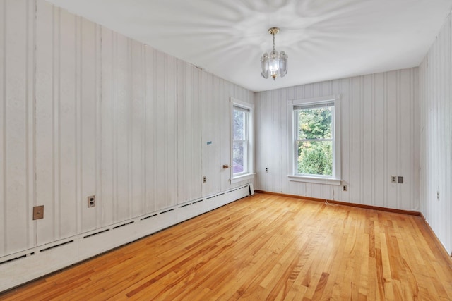 empty room featuring a notable chandelier, light hardwood / wood-style floors, and a baseboard radiator