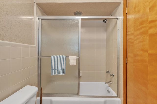 bathroom featuring toilet, enclosed tub / shower combo, and tile walls