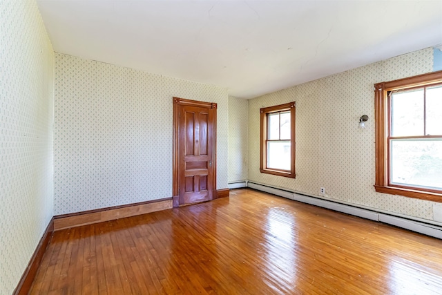 empty room with hardwood / wood-style floors, wallpapered walls, and a baseboard heating unit