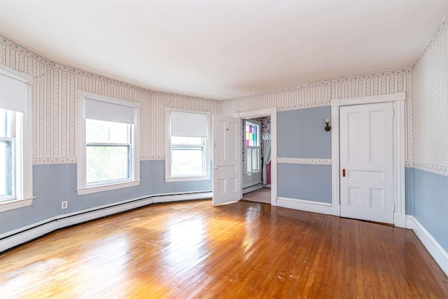 spare room with hardwood / wood-style floors, wallpapered walls, baseboard heating, and a healthy amount of sunlight