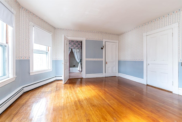 unfurnished bedroom featuring hardwood / wood-style flooring, baseboards, a baseboard heating unit, and wallpapered walls