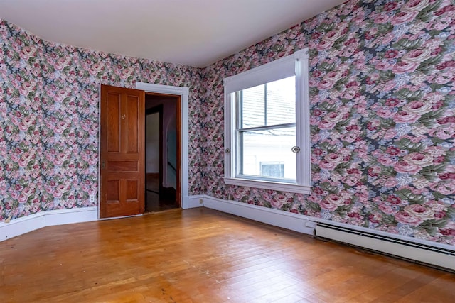 spare room featuring a baseboard heating unit, wallpapered walls, and light wood-style floors