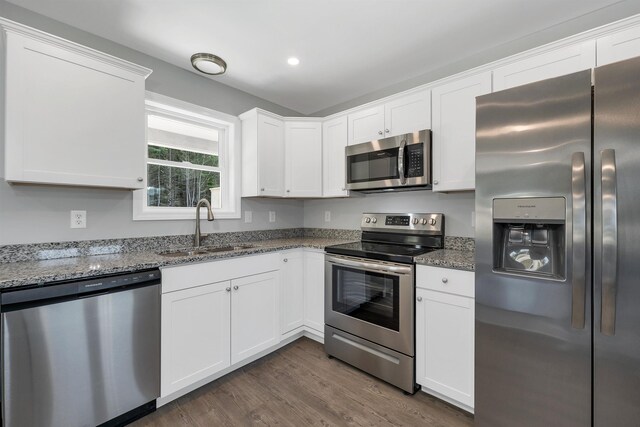 kitchen featuring dark wood-type flooring, a sink, appliances with stainless steel finishes, white cabinets, and stone counters