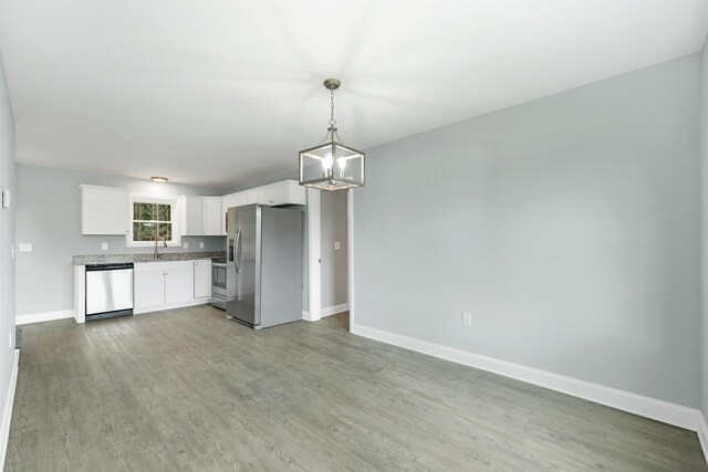 kitchen featuring light wood-type flooring, pendant lighting, appliances with stainless steel finishes, white cabinets, and baseboards