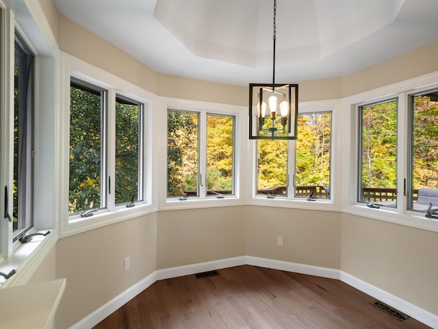 unfurnished sunroom featuring a tray ceiling, plenty of natural light, and a chandelier