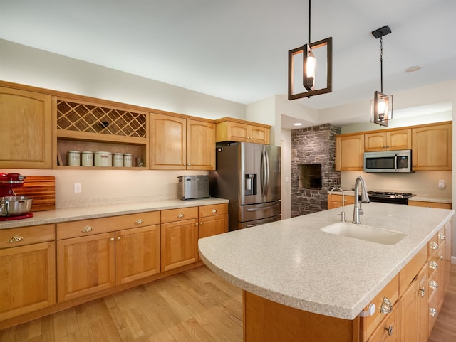 kitchen with appliances with stainless steel finishes, light wood-type flooring, sink, a center island with sink, and hanging light fixtures