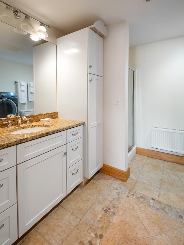 bathroom featuring vanity, a shower with door, radiator heating unit, and washer / clothes dryer