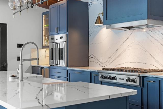 kitchen with extractor fan, blue cabinetry, decorative backsplash, light stone countertops, and appliances with stainless steel finishes