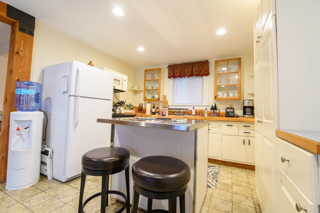 kitchen featuring white appliances, stainless steel counters, white cabinets, and a kitchen bar