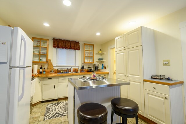 kitchen featuring stainless steel counters, white cabinets, a breakfast bar, sink, and white refrigerator