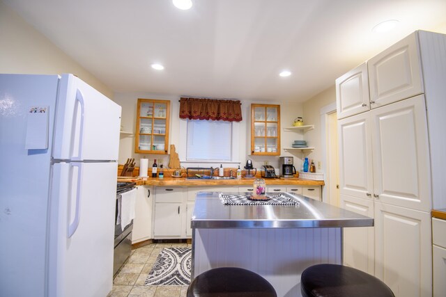 kitchen with black range with electric stovetop, stainless steel counters, sink, white fridge, and white cabinetry